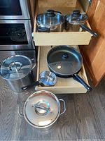 Cooking pots and pans shown in drawers and on floor with lids, various sizes and materials.