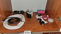 Photo showing two power banks, multiple charging cords including USB cables, three black USB wall chargers, white DSL cable, and wired earbuds all placed on a wooden shelf.