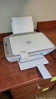 HP Deskjet 2755e printer showing paper input tray at the rear and output paper tray extended in front, white and gray color.