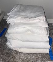 Stack of white folded twin sheets consisting of fitted and flat sheets on carpeted floor