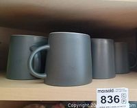 Seven matte gray ceramic coffee mugs in a row on a shelf, front view showing handles.