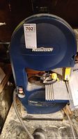 Front angled view of the blue Mastercraft 9-inch band saw with instruction manual in background and sticker with lot number attached.