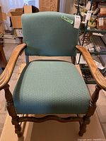 Front view of the green upholstered wooden armchair with visible nailhead trim