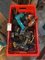 Overhead view of red tote bin filled with various power tools, batteries, and chargers showing overall condition and lot contents.