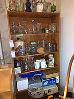 Seven shelves filled with various glassware, mugs, bowls, trays, wood cutlery case, and boxes on bottom shelf