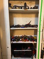 Full view of storage shelves showing hand planes on top, saws, screwdrivers, pliers, clamps, staplers and baskets.