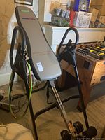 Full view of inversion table showing grey padded backrest, black frame, resistance bands and ankle support.