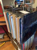 Plastic case filled with assorted vinyl records placed upright showing edge of album covers and some aged paper sleeves.