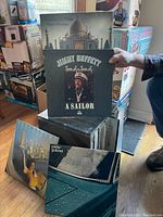 Photo showing a plastic case holding multiple vinyl records with visible covers including Jimmy Buffett's 'A Sailor' and other various artists.