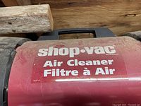 Red cylindrical Shop Vac air cleaner filter housing with white text labeling on the side.