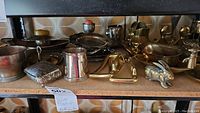 Shelf with various silver-plated items including plates, cup, brass animal figurines, and a small box.