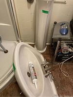 White oval pedestal sink with faucet installed, showing the basin with a tube of caulking inside and the drain hole.