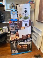 Stack of boxed small appliances including glass precision chopper, coffee grinder, bread maker, and toaster oven.