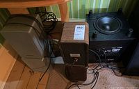 Photo showing the pair of beige Optimus STS50AV speakers, small brown Realistic speakers, and black Advent AHT850 subwoofer side by side on floor.