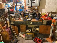 Full view of workbench top shelf, showing various hand tools such as screwdrivers, pliers, measuring tools, and hardware items. Cabinets underneath workbench are open, showing more tools and a toolbox.