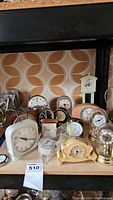 Photo of entire collection of 13 vintage clocks arranged on wooden surface with patterned wallpaper background.