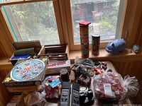 Overall assortment on table by window, showing Sta-Lox tube, cylinder of discs, Minubrix puzzle box, bags of bricks and hardware, diecast cars, radio, pig bank