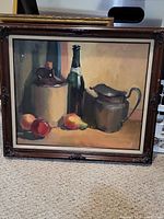 Full view of vintage painting showing bottle, pitcher, and fruit still life with wooden frame on beige carpet