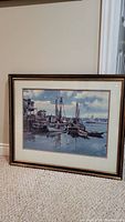 Full framed picture resting on floor showing fishermen boats at dock and harbor scene.