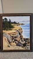 Full view of the framed coastal landscape painting depicting cliffs, ocean, and trees.