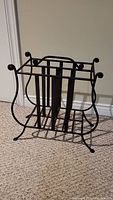 Front view of black metal magazine rack showing scrollwork and handle design.