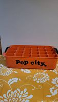 Front side view showing orange color, black Pop City logo, and black handles.