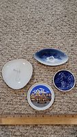 Four small collectible plates displayed on carpet with measuring ruler showing sizes between 3 to 4 inches.