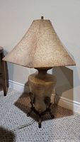 Full view of the entire lamp showing the beige ceramic base and the wide beige fabric lampshade with a slightly flared shape.