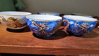 Six vintage teacups in total displayed, five blue and one white, showing dragon designs and shaped handles.