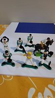 Seven Wilton baseball player cake topper figurines and one horse rider figurine arranged on white and blue background