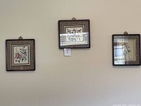 Set of three framed silk embroidered artworks hung on a wall.