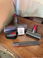 Four Dyson vacuum attachments on a wooden surface showing floor spot duster, pet hair tool, crevice tool and brush attachment.