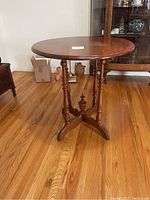 Side view of the antique mahogany round table showing the circular top and turned legs connected with cross stretchers and central finial.