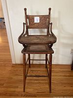 Full front view of antique oak high chair showing wood frame, woven cane seat, and solid wood backrest panel with a sticker '25' attached.