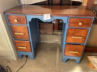 Front view of child's solid wood desk showing blue frame, wood top, and six drawers with brass hardware.
