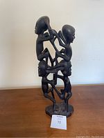 Full view of the ebony wood sculpture depicting multiple human figures intertwined vertically.