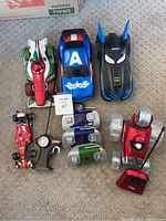 Lot of 5 R/C cars displayed on carpet floor showing the character cars from Ridemakerz, several remotes, and the Turbo Tumbler car with red remote.
