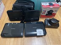 Six electronic items arranged on floor: 2 Philips portable DVD players, 2 Sylvania portable DVD players, Foscam IP camera box, Fujifilm Instax instant camera