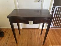 Closed vintage wooden side table with curved edges and tapered legs on hardwood floor.