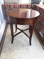 Front view showing round wooden table with one drawer and curved legs connected by an X-shaped stretcher.