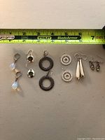 Full lot view of six pairs of earrings with a measuring tape for scale showing approximately 2-3 inches in total length per earring.