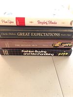 Four hardback books stacked horizontally showing titles and spines: Bergdorf Blondes, Great Expectations, The Second Skin, Fashion Buying and Merchandising.