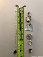 Photo showing a silver chain necklace with an oval garnet stone pendant alongside five loose pendants and a measuring tape for size reference.