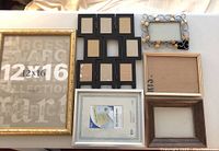 Overall assortment of seven picture frames of various sizes and styles laid out on fabric for display.