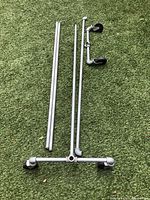 Dismantled metal pipe parts including two vertical uprights, a horizontal base with casters, and additional caster assembly