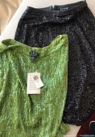 Green sequined mini skirt and black sequined pencil skirt laid flat showing full items