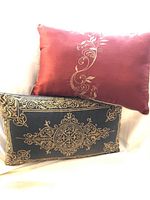 Two throw pillows, one dark green with gold embroidery and zipper, one rust colored with beige/taupe embroidery, displayed together