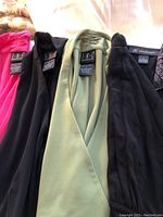 Close-up view of four sleeveless tops showing black, green, and hot pink colors, brand INC labels visible on three tops.