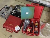 Overview of two red plastic cases open showing emergency kits including flares, light, first aid kit, and air inflator can along with Plus start booster cables box.