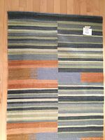 Blue, orange, beige and grey striped wool runner rug with block stripe patterns, folded and placed on wood floor.
